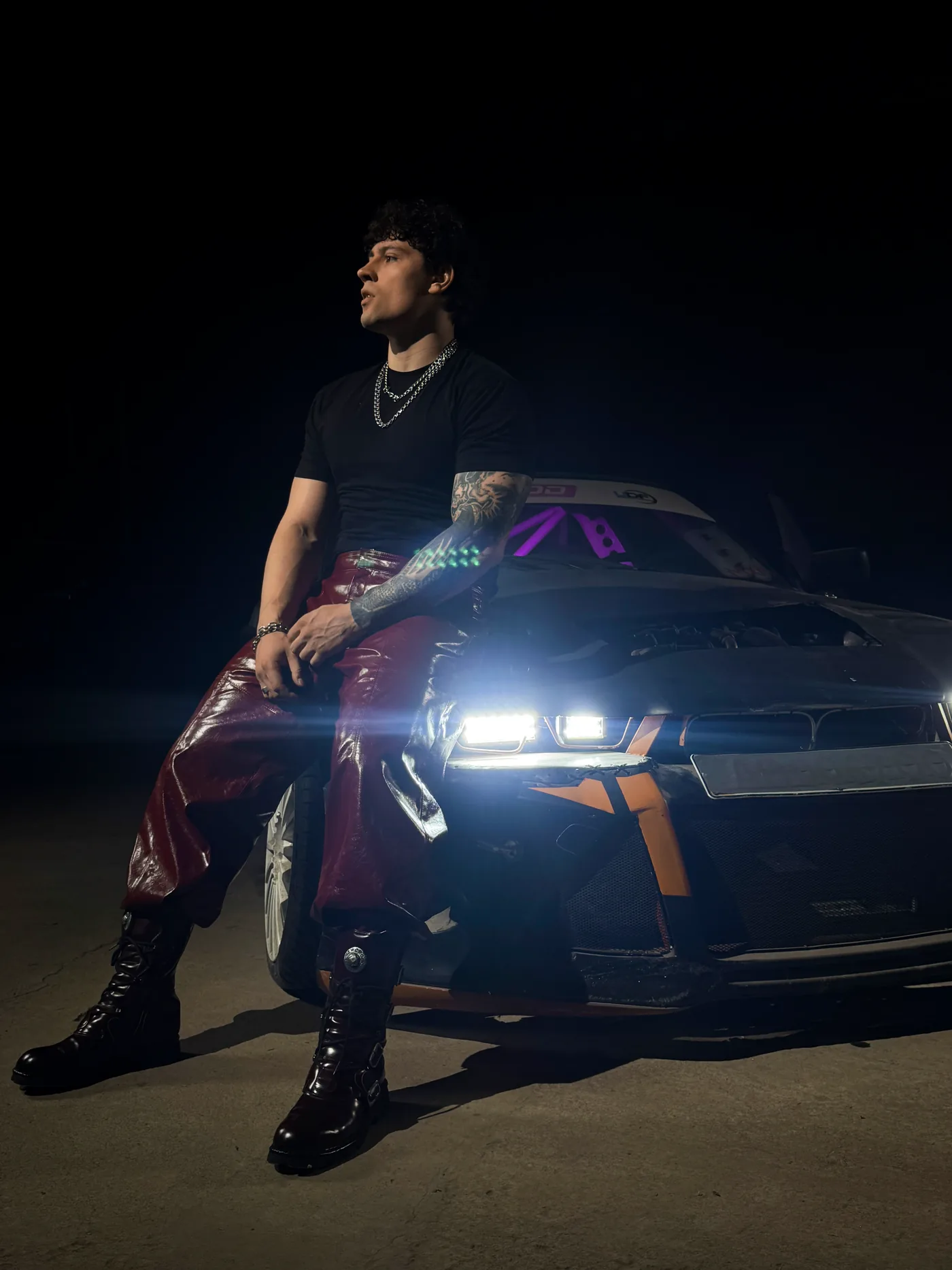 DISTEYO sitting on the hood of a car at night, headlights on
