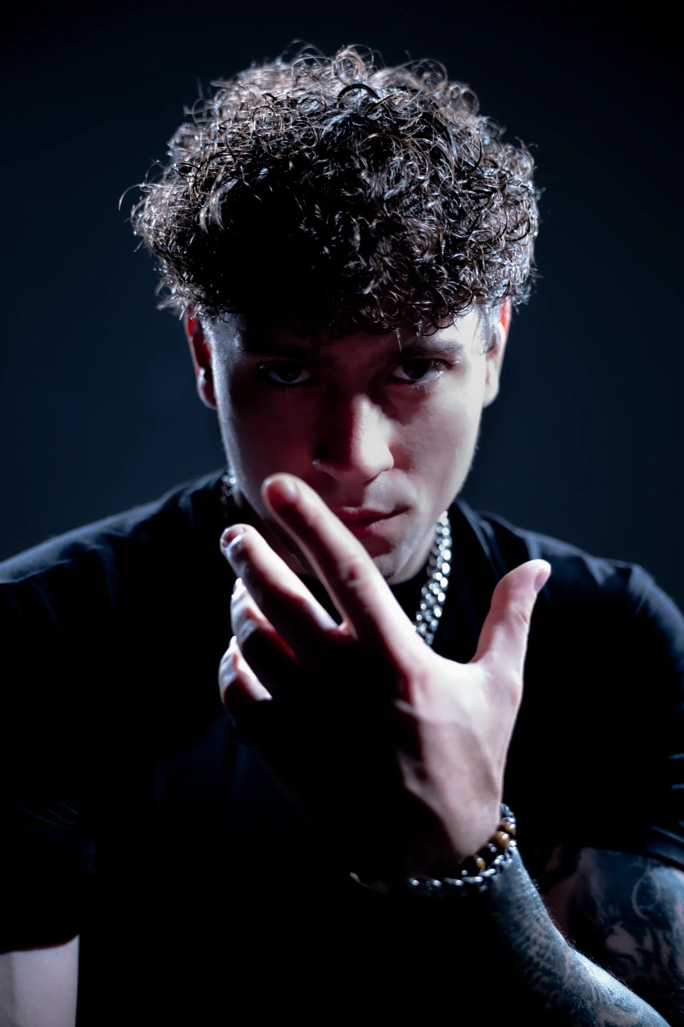 DISTEYO reaching a hand toward the camera, chains at his neck