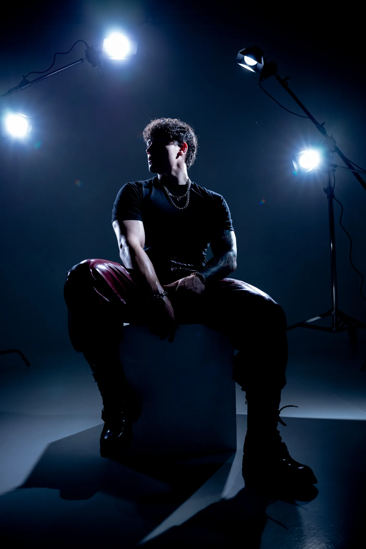 DISTEYO seated on a cube in a studio, lit by three spotlights